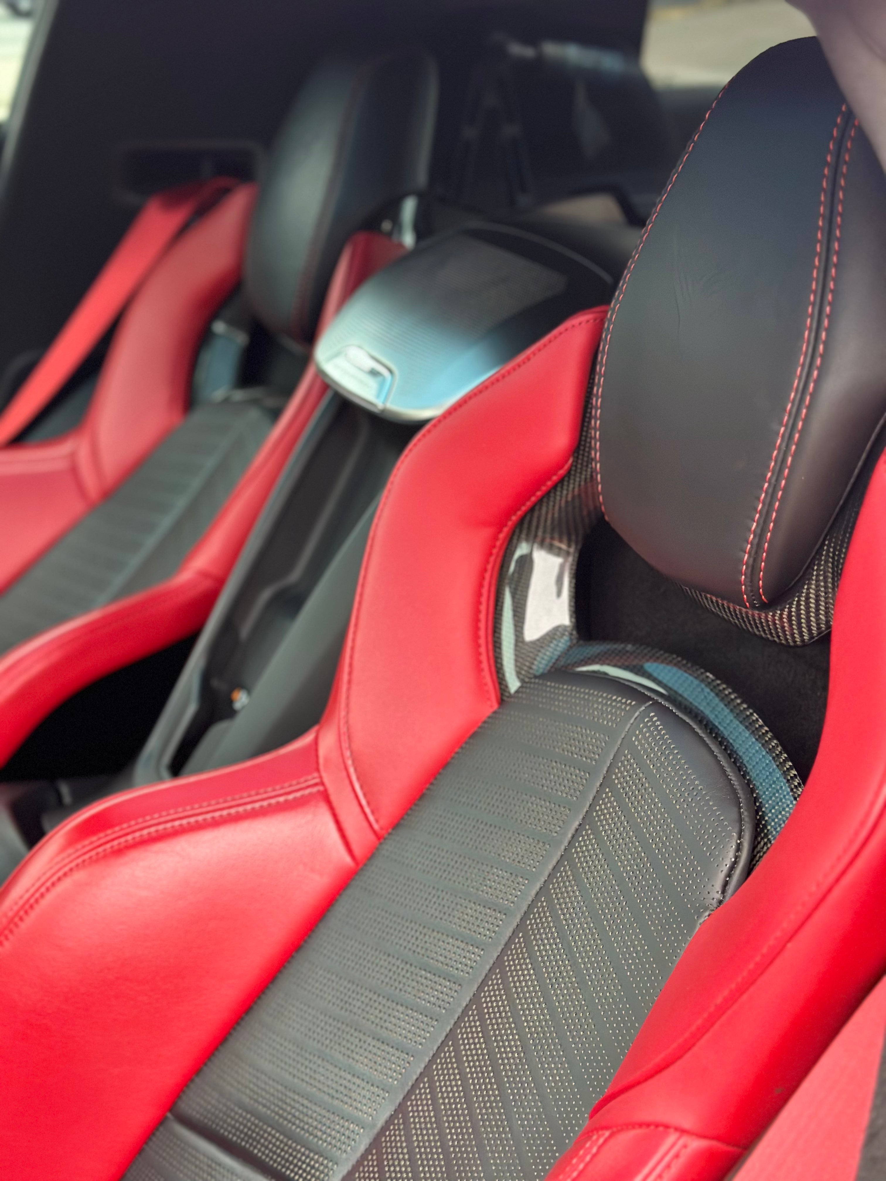 C8 Corvette interior view from back seats to front, highlighting premium red leather seats, advanced dashboard, and driver-focused cockpit.