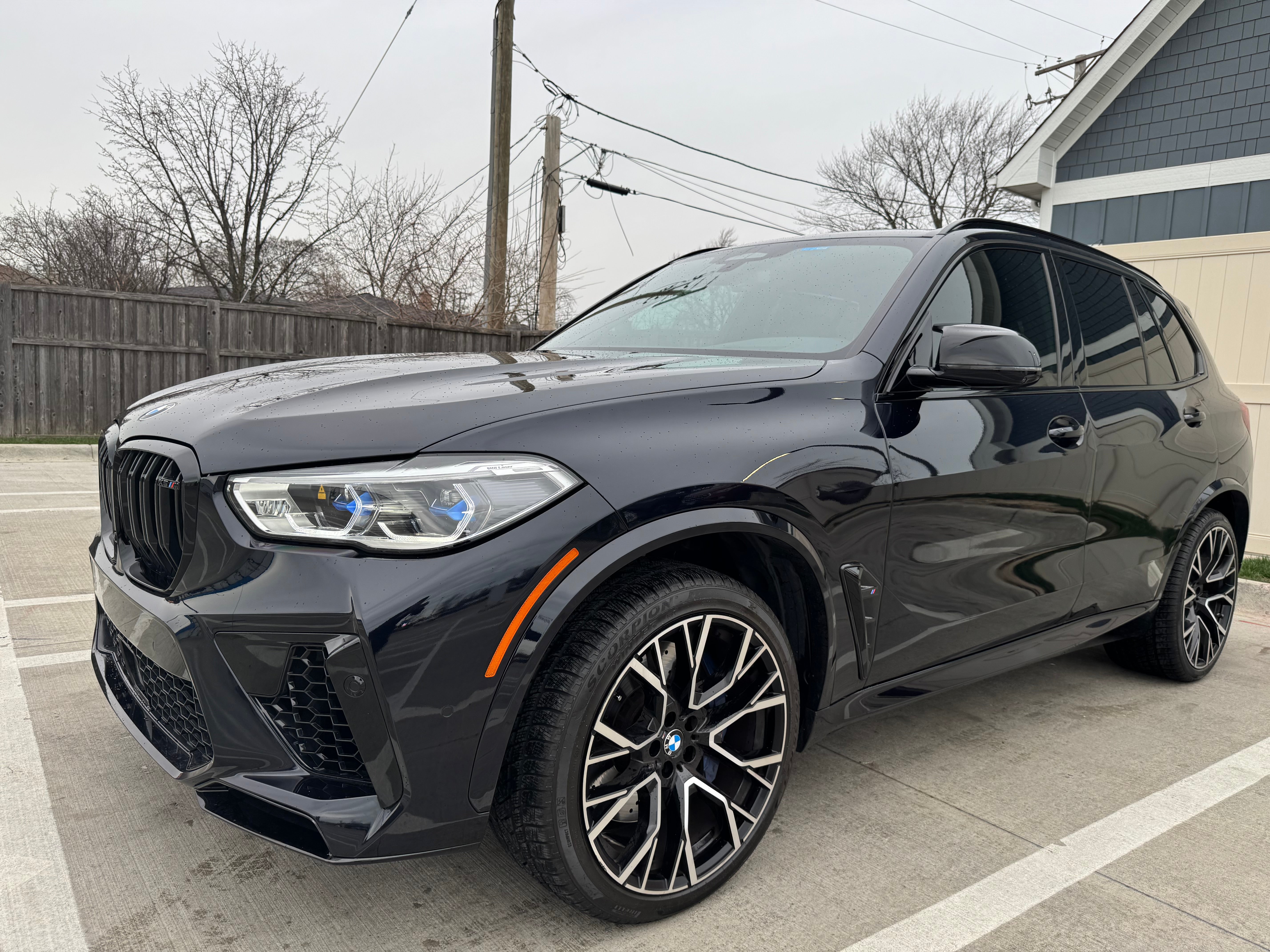 MW X5M Competition front driver-side corner view with a close-up of the premium alloy wheel, bold grille, and sleek aerodynamic design.